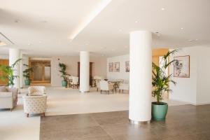 un vestíbulo con columnas blancas, sillas y mesas en Hipotels Bahía Grande Aparthotel en Cala Millor