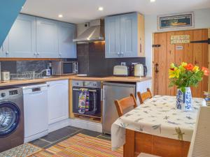 a kitchen with blue cabinets and a table with a vase of flowers at Puffin Cottage in Abereiddy