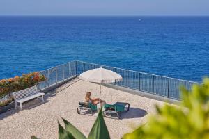 a woman sitting on a chair under an umbrella next to the ocean at Golden Residence Hotel in Funchal
