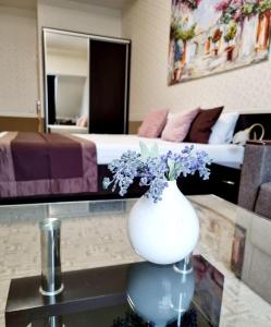 a white vase with purple flowers on a table in a bedroom at TipTop Hotel CITY CENTER in Chişinău