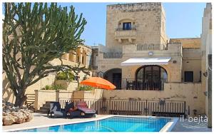 a pool with chairs and an orange umbrella next to a building at Il-Bejta Farmhouse in Għarb +30 photos