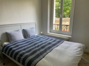 a bed with a blue and white comforter and a window at CHARMING APARTMENT WITH THE PRIVATE GARDEN in Orsay