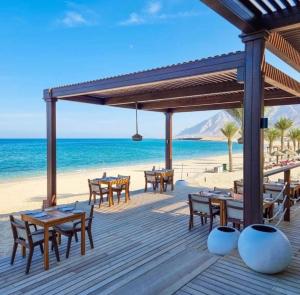 Beach front Le Bon villa في مسقط: سطح خشبي مع طاولات وكراسي على الشاطئ