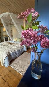 a vase with purple flowers on a table next to a bed at Cosy guesthouse with sauna and outdoor kitchen in Kuressaare