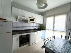 kuchnia z białymi szafkami, stołem i kuchenką mikrofalową w obiekcie Apartamento Dicar w mieście Foz