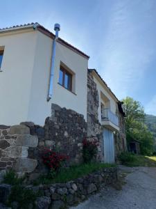 una casa bianca con un muro in pietra e fiori di Farm house in Ribeira Sacra a O Carballo