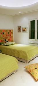 2 Betten in einem Zimmer mit gelber Bettwäsche und Fenstern in der Unterkunft Chambres d'hôtes Conviviales avec piscine privée Chambre Namasté et Chambre Rose des Sables in Djerba