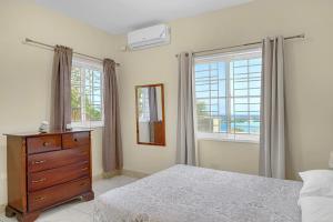 a bedroom with a bed and a dresser and windows at Palm Leaf Cottage in Montego Bay