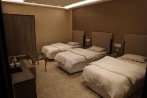 a hotel room with three beds and a table at Al Shaiki Hotel in Al Jubail