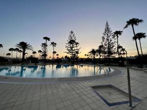 ein großer Pool mit Palmen und Sonnenuntergang in der Unterkunft Beach Cottage in Maspalomas