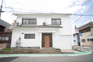 a white house with a brown door on a street at Yokkaichi Kawaramachi Hotel in Hazu