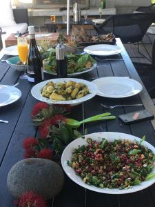 drewniany stół z talerzami jedzenia i butelkami wina w obiekcie Medlands Beach House na wyspie Great Barrier Island