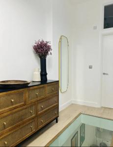 a dresser with a mirror and a vase of flowers on it at Gorgeous split level Belsize Park Apartment in London