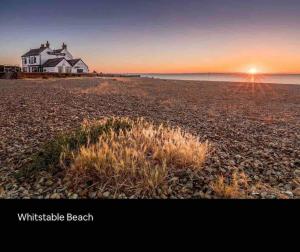 a house on a rocky beach with the sun setting at Whitstable, CW18, 2 bed park home, Alberta Holiday Park in Seasalter