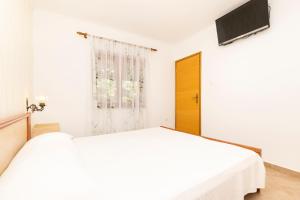 een witte slaapkamer met een bed en een televisie aan de muur bij Apartments Dominik in Mali Lošinj