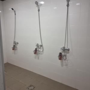 a bathroom with three shower systems on a white wall at Camp Genys in Jurbarkas