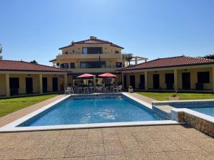 a swimming pool with tables and chairs in front of a building at Quinta Dos Amarelos no Meco in Aldeia do Meco