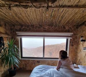 una mujer sentada en una cama mirando por la ventana en Dana’s Trail Hotel, en Dana