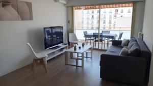 ein Wohnzimmer mit einem Sofa, einem TV und einem Tisch in der Unterkunft Superbe T3 L’Illiade - Plages 3’ à pieds - Parking in Juan-les-Pins