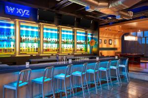 un bar con taburetes azules en una habitación con alcohol en Aloft Hotel Las Colinas, en Irving