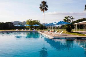 Maracay的住宿－Marriott Maracay Golf Resort，一个带蓝色遮阳伞的大型游泳池,且有人坐在椅子上