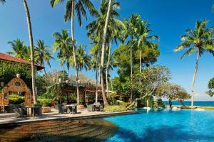 een zwembad in een resort met palmbomen en de oceaan bij Sheraton Senggigi Beach Resort in Senggigi 