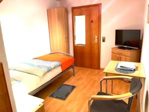 Habitación pequeña con cama, escritorio y TV. en Pension Waldau, en Kassel