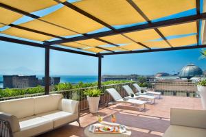 un patio con muebles blancos y vistas al océano. en Renaissance Naples Hotel Mediterraneo, en Nápoles