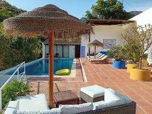 a villa with a pool and a straw umbrella at B&B rural El Oasis in Almuñécar