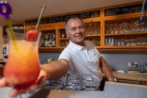 un homme derrière le comptoir d'un bar avec un verre dans l'établissement Naturhotel Feriengut Darrehof, à Serfaus