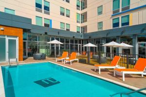 a swimming pool with orange chairs and a building at Aloft College Station in College Station