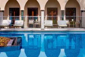 einen Pool mit Stühlen und einem Tisch in der Unterkunft Al Bustan Palace, a Ritz-Carlton Hotel in Muscat