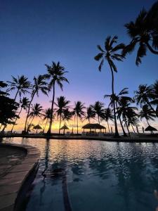 a swimming pool with palm trees and a sunset at Bitingui Praia Hotel in Japaratinga