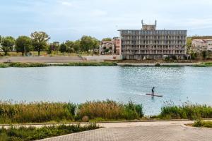 a person on a paddle board in a lake with a building at Hotel CASA ROYAL pe plaja Belona in Eforie Nord