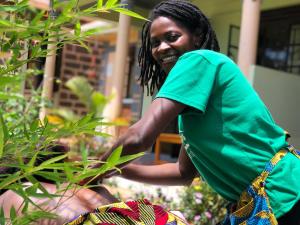 Una donna con una camicia verde in piedi accanto a una pianta di Home of Friends a Kapchorwa