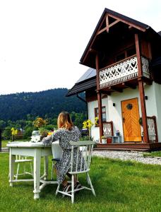 une femme assise à une table devant une maison dans l'établissement Gazdówka - najlepsza miejscówka domek w Pieninach, à Krościenko nad Dunajcem