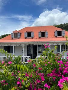 una casa bianca con tetto arancione e fiori rosa di Habitation La Reine du Camp Chambres d'Hôtes a Saint-Claude
