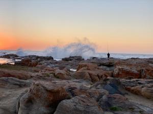 un hombre parado en una playa rocosa con olas y ondulaciones en Uvongo Cabanas 15B, en Margate