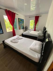 two beds in a room with red curtains at Hostal Recuerdos del Tayrona in El Zaino