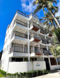 a white building with balconies and a palm tree at Si! Coral Inn in Thulusdhoo