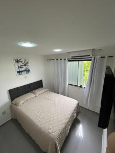 a white bedroom with a bed and a window at Apartamento na Praia de Guaibim in Guaibim