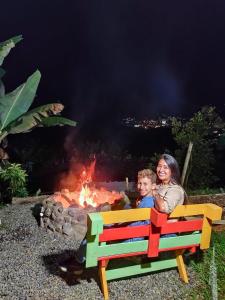 une femme et un enfant assis sur un banc à côté d'un feu dans l'établissement Casa Viva Alojamiento Rural, à Jardín