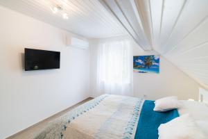 a white bedroom with a bed and a tv at Eternity Apartmanház in Keszthely