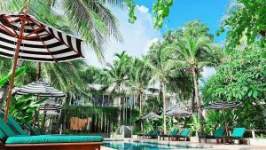 シャロンにあるSignature Phuket Resort SHA Plusのヤシの木が茂るプール(椅子、パラソル付)