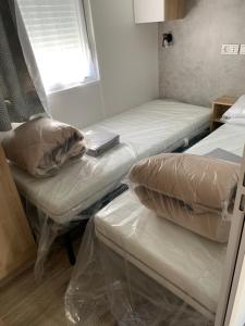 Cette chambre comprend 2 lits, un oreiller et une fenêtre. dans l'établissement Envie d un break de paysages sauvages et de nature ce mobile home neuf tout confort climatise idealement situe au bord de l eau dans un camping 4 etoiles vous attend pour un week end quelques jours ou des vacances en famille, à Cap-Ferret