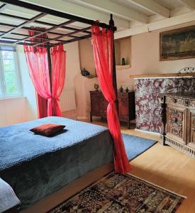 1 dormitorio con 1 cama con cortinas rojas y chimenea en Manoir normand du XIVe siecle., en Le Lorey