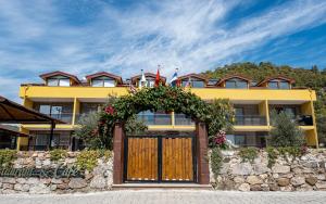 ein gelbes Gebäude mit einer Holztür und Blumen in der Unterkunft Olive Tree Apart Hotel in Muğla