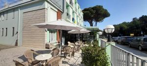 una cafetería al aire libre con mesas, sillas y sombrilla en Hotel Maddalena, en Marina di Ravenna