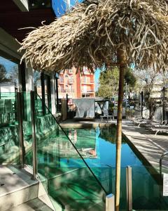 a swimming pool with a straw umbrella next to a building at Hotel Montecarlo - Vista Mare con Piscina & Area Fitness in Riccione