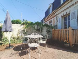 um pátio com uma mesa, cadeiras e um guarda-sol em La Maison des Magnolias em Trouville-sur-Mer